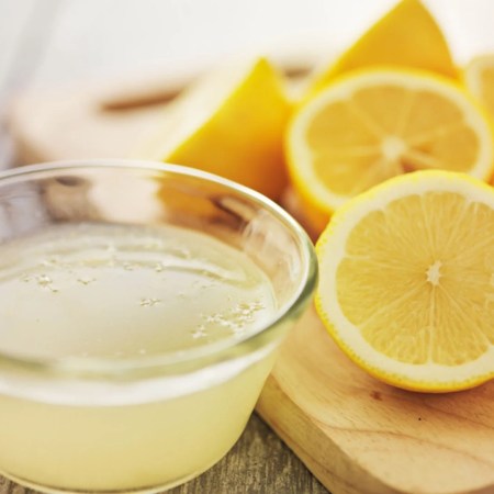 Bir bardak ılık limonlu su ve yanında dilimlenmiş taze limonlar